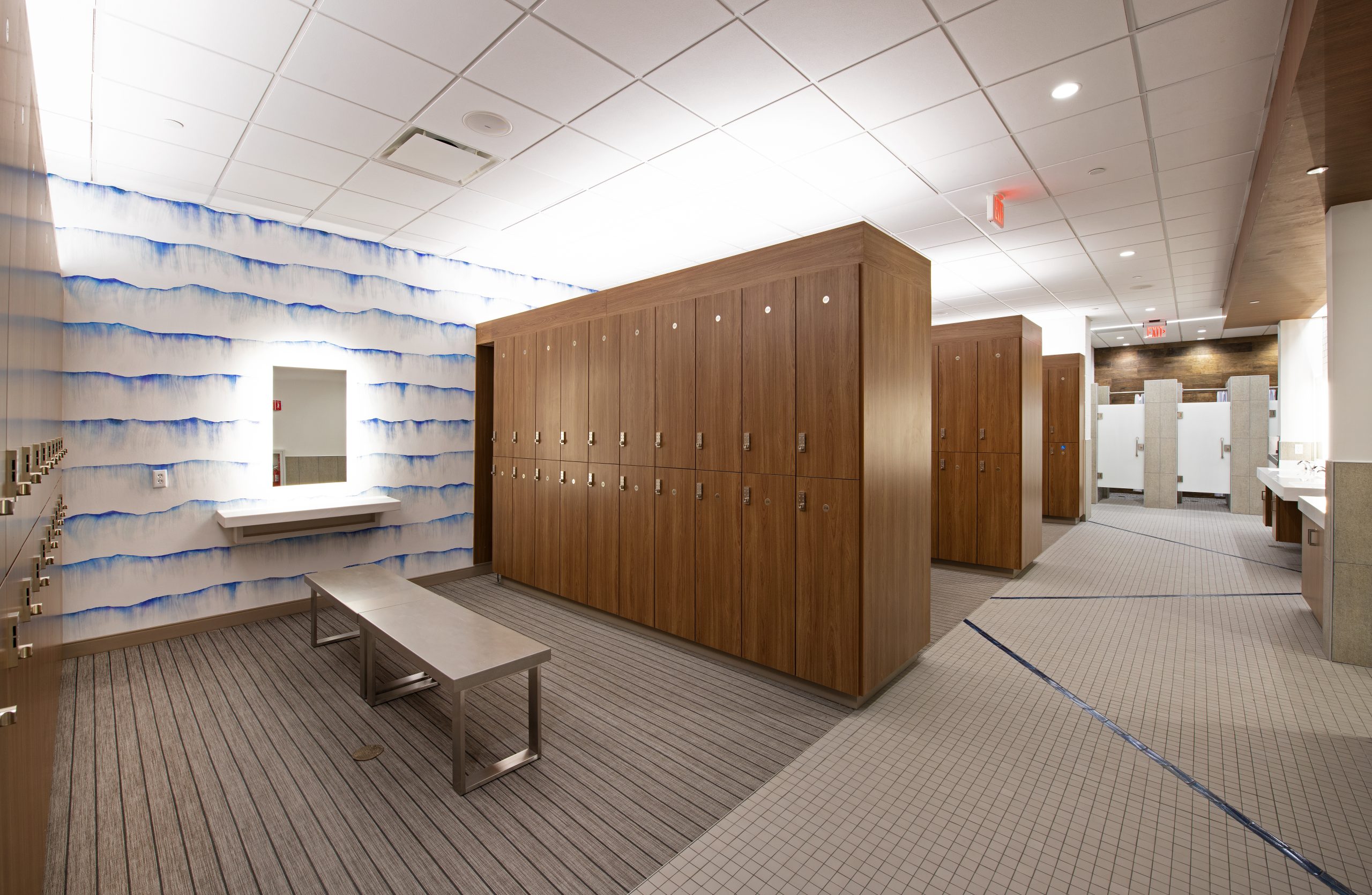 Spacious locker room vanity area at Lake Nona Performance Club featuring warm wood cabinetry, backlit mirrors, and premium wood-finish lockers — part of the steam and sauna locker room amenities in Lake Nona, FL